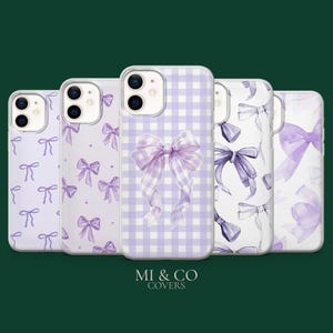May include: A collection of five phone cases with various designs. The cases feature a light purple color scheme with bow patterns. One case has a gingham pattern with a large bow. The cases are arranged in a row against a dark green background.