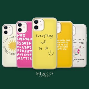 Puede incluir: Una colección de cinco fundas para teléfonos con citas y diseños inspiradores. Las fundas son de varios colores, incluyendo blanco, rosa, amarillo y naranja. Cada funda presenta un diseño y texto únicos, como un sol, una carita sonriente y frases motivadoras.