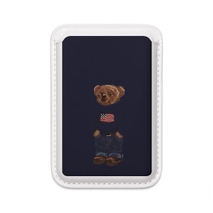 May include: Navy blue phone case featuring a teddy bear wearing a sweater with an American flag design and blue jeans. The bear has brown fur and is wearing brown shoes. The case has a white border.