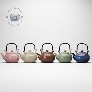 Może przedstawiać: Pięć ceramicznych czajniczków w rzędzie, każdy w innym kolorze i z drewnianym uchwytem. Kolory obejmują różowy, beżowy, brązowy, zielony i niebieski. Czajniczki mają klasyczny design i prawdopodobnie służą do parzenia herbaty.
