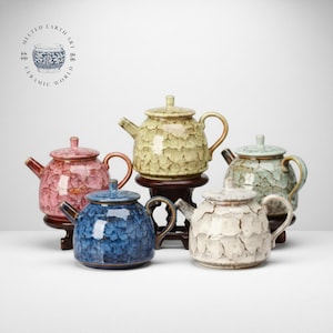 May include: A collection of ceramic teapots in various colors, including pink, blue, green, and white. Each teapot has a textured surface and is displayed on a wooden stand. The teapots have a classic design with a spout, handle, and lid.