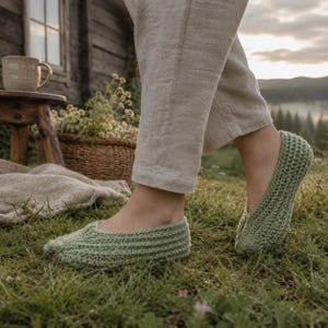 Puede incluir: Un par de zapatillas de ganchillo verde claro. Las zapatillas se usan sobre una superficie cubierta de hierba. Las zapatillas tienen un aspecto texturizado y un diseño de punta redondeada. La persona lleva pantalones de color claro.