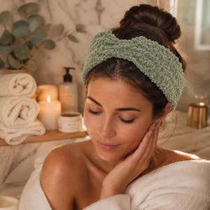 May include: A sage green, textured headband is worn by a person in a white robe. The headband is made of a soft, plush material. The background includes candles, towels, and bath products, suggesting a spa or self-care theme.