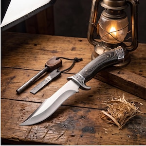 May include: A hunting knife with a silver blade and a dark wood grain handle. A fire starter and a metal striker are next to the knife. A vintage lantern and a small pile of straw are in the background. The knife has a decorative metal bolster.