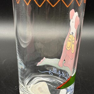 May include: Clear glass tumbler with an orange zig-zag design around the rim. The glass features a cartoon dog illustration in pink, white, and yellow. The dog is sitting on a green mat. The word "jellyfish" is written on the glass.