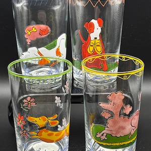 May include: Set of four clear drinking glasses with colorful dog illustrations. Each glass features a different dog design, with accents of blue, orange, green, and yellow rims. One glass has the text "what a" and another has "the lap of".