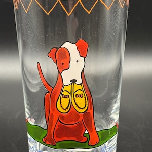 May include: Clear glass tumbler with a cartoon dog illustration. The dog is red with white markings and yellow shoes. The rim has an orange zig-zag design. The words "Faithfully" are written at the bottom of the glass.