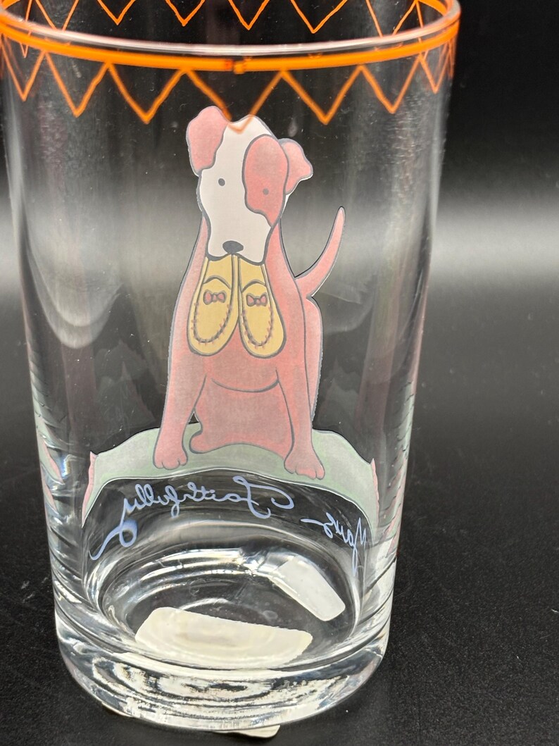 May include: Clear glass tumbler with an orange geometric design at the rim. The tumbler features a pink dog illustration with a white face and yellow shoes. The words "fully committed" are written in cursive on the glass.