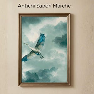 May include: Framed artwork featuring a crane in flight against a cloudy, teal-colored sky. The bird has white and blue wings, and the frame is a warm, metallic gold color. The text "Antichi Sapori Marche" is at the top.