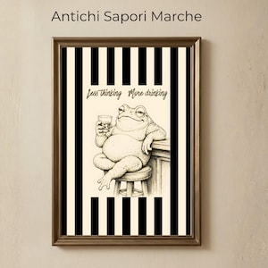 Può includere: Stampa artistica incorniciata con un cartone animato di una rana che tiene in mano un drink, con la scritta "Less thinking More drinking". Lo sfondo presenta strisce verticali bianche e nere. La cornice è marrone.