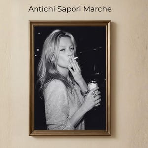 Può includere: Stampa incorniciata in bianco e nero con una donna che fuma una sigaretta e tiene in mano una lattina. La stampa è in una cornice color oro ed è montata su una parete beige. Il testo "Antichi Sapori Marche" è in alto.