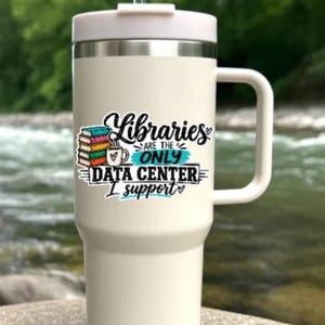 May include: A cream-colored insulated tumbler with a handle, a lid, and a clear straw. The front features a graphic of a stack of colorful books, a coffee mug, and the text: Libraries are the only data center I support, written in black and teal.
