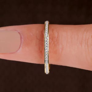 Könnte beinhalten: Ein dünner Goldring mit Kanalfassung, der eine durchgehende Reihe kleiner, klarer, rund geschliffener Steine auf der Außenfläche aufweist. Das Metall hat eine polierte Oberfläche und die Steine sind in einer geraden Linie angeordnet.
