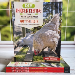 May include: A stack of three red and white paperback books titled "DIY Chicken Keeping From Fresh Eggs Daily" by Lisa Steele. The front cover features a close-up of a white chicken pecking at the ground.