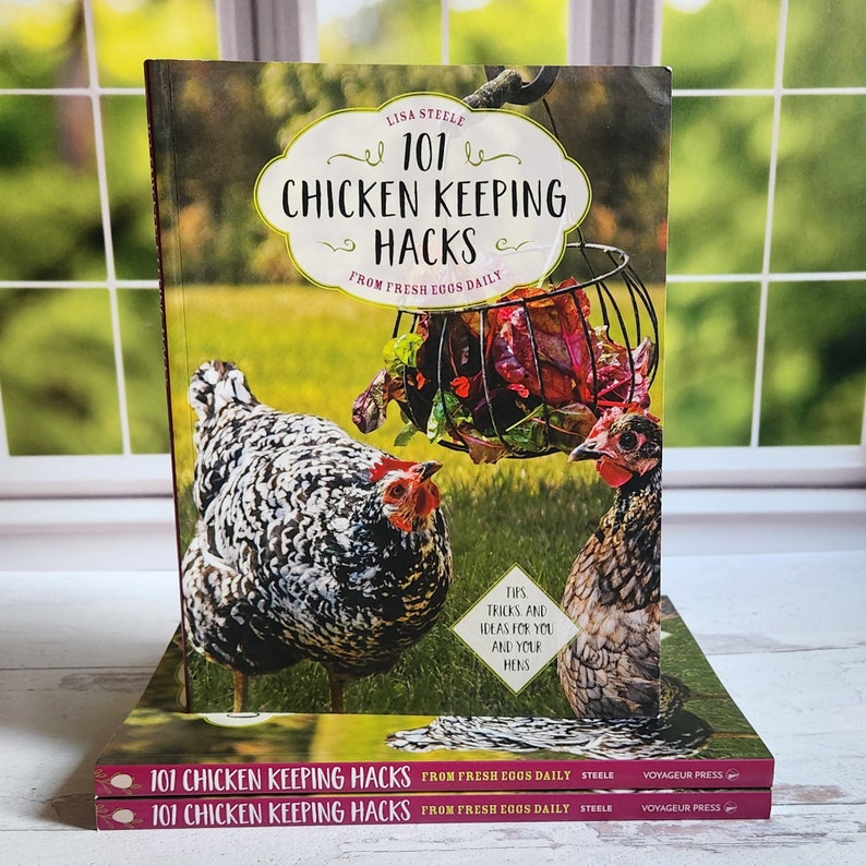 May include: A stack of three books titled "101 Chicken Keeping Hacks" by Lisa Steele. The cover features two chickens and a basket of leafy greens.