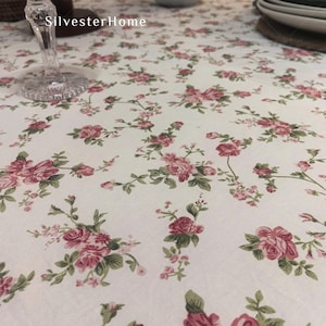 Puede incluir: Un mantel blanco con un patrón repetido de rosas rosas y hojas verdes. El diseño floral cubre toda la superficie, creando una estética vintage. El texto "SilvesterHome" es visible en la esquina superior izquierda.