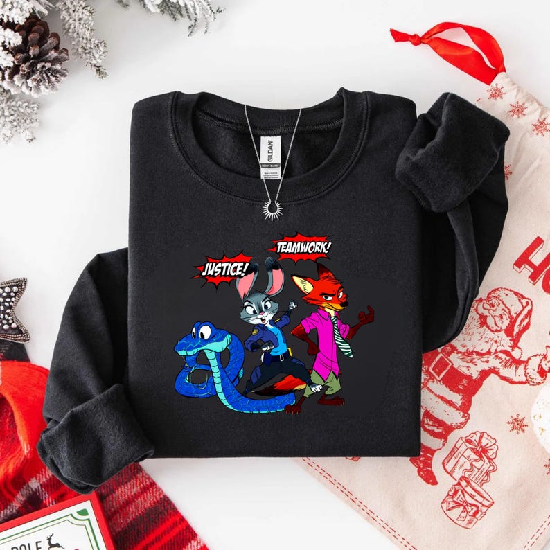 May include: Black crewneck sweatshirt featuring a cartoon illustration of a blue snake, a gray bunny, and a red fox. The words "JUSTICE!" and "TEAMWORK!" are in speech bubbles. A silver necklace is visible.