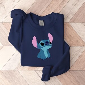 Puede incluir: Sudadera azul marino con una ilustraci&oacute;n de Stitch de Lilo & Stitch. El personaje est&aacute; representado en tonos azules con grandes ojos negros y orejas rosas. La sudadera est&aacute; hecha de un material suave y es adecuada para uso casual.