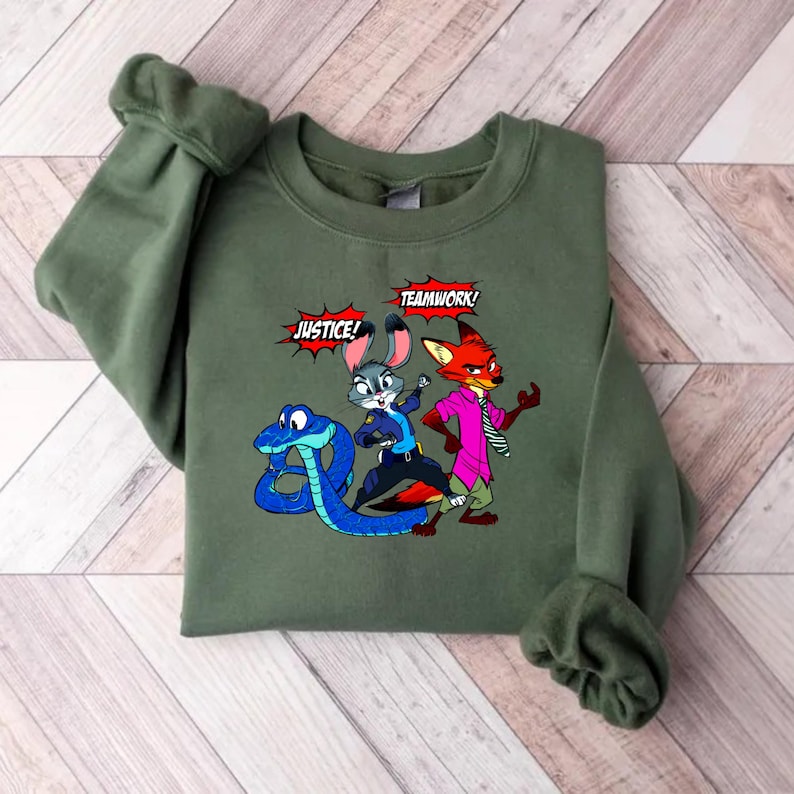 May include: An olive green sweatshirt featuring a cartoon graphic of a blue snake, a gray bunny in a police uniform, and a red fox in a pink shirt. The words "JUSTICE!" and "TEAMWORK!" are in speech bubbles.