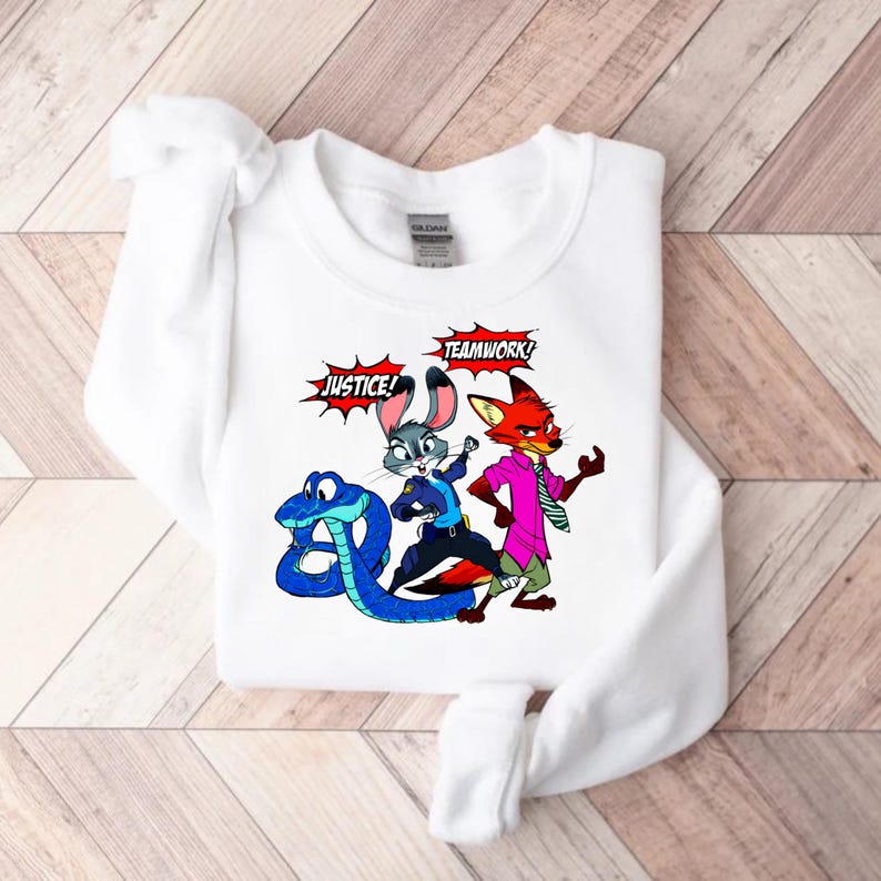 May include: White sweatshirt featuring a colorful cartoon graphic of characters from Zootopia. The design includes a blue snake, a gray rabbit, and a red fox, with the words "JUSTICE!" and "TEAMWORK!" in speech bubbles.