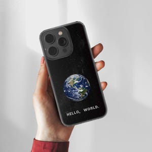 Op de afbeelding: Zwarte telefoonhoes met een sterrennachtontwerp en een gedetailleerde afbeelding van de aarde. De telefoonhoes heeft de woorden "HELLO, WORLD." in het wit onderaan gedrukt.