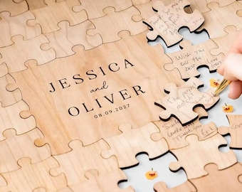 May include: A wooden puzzle guest book with the names "JESSICA and OLIVER" and the date "08.09.2027" printed on it. Several puzzle pieces are missing, and some are signed with well wishes. A hand is holding a pen.