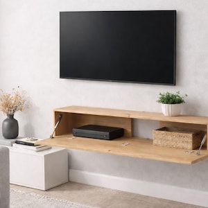 May include: A contemporary wall-mounted media unit in light wood. It has a drop-down door, a black media player, and a woven basket. A black flat-screen TV is mounted above. A small potted plant and a decorative vase are also visible in the image.