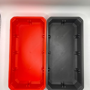 May include: Two rectangular open containers, one bright orange and one dark gray, positioned side-by-side. Each container features a flat base, vertical walls with a beveled inner rim, and small structural tabs along the interior sides.