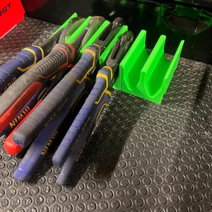 May include: A collection of Irwin Vise-Grip pliers with red, blue, and black handles, alongside a bright green tool organizer. The pliers are arranged on a textured, dark surface, suggesting a workshop or tool storage setting.