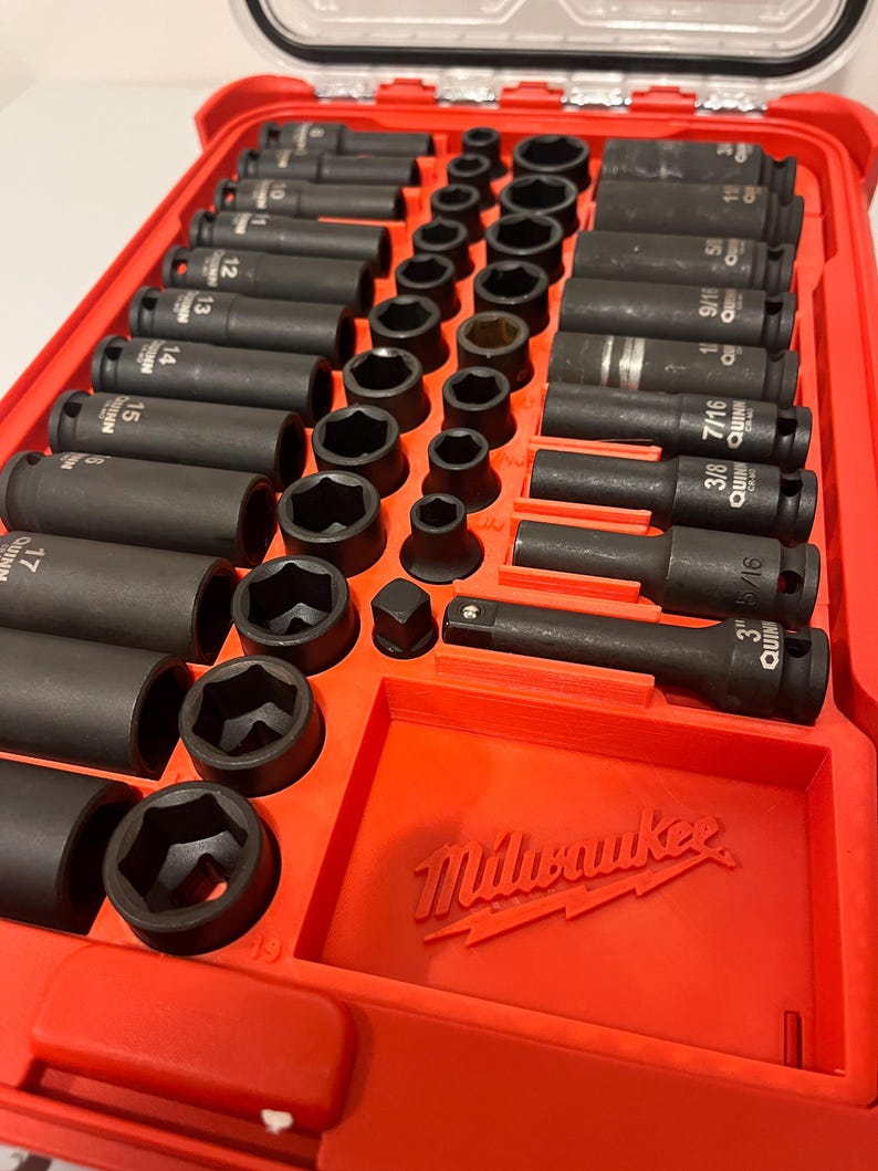 Puede incluir: Una caja de herramientas roja llena de un juego de vasos y extensiones de impacto negros. Los vasos est&aacute;n dispuestos en filas y etiquetados con tama&ntilde;os en mm. La caja de herramientas tiene el logotipo de Milwaukee.