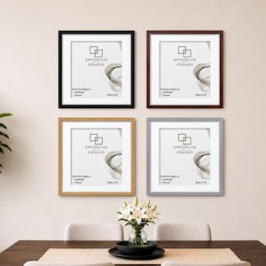 May include: Four framed prints in black, brown, gold, and grey, each with a white mount and the text "Emporium Frames." The frames are hung on a neutral wall above a dining table with a floral centrepiece.