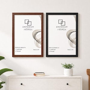 May include: Two rectangular picture frames, one brown and one black, are displayed on a white wall. Each frame has a white interior with a graphic design and text. A white cabinet with a plant and a wooden chair are in the foreground.