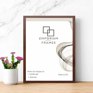 May include: A framed print with a dark brown wooden frame. The print features the text "EMPORIUM RETAIL FRAMES" and a decorative swirl design. The frame is suitable for landscape and portrait display. A small white vase with pink flowers is in the foreground.