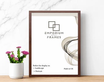 May include: A framed print with a dark brown wooden frame. The print features the text "EMPORIUM RETAIL FRAMES" and a decorative swirl design. The frame is suitable for landscape and portrait display. A small white vase with pink flowers is in the foreground.