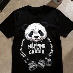 Może przedstawiać: Czarny t-shirt z pandą w bluzie z kapturem i butach sportowych. Grafika pandy zawiera biały napis "Napping is my Cardio". Biała butelka na wodę z czarnym napisem jest widoczna w tle.