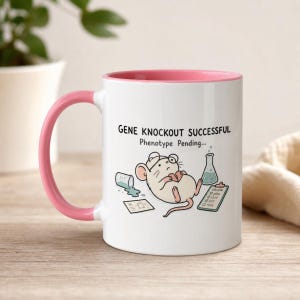 Könnte beinhalten: Ein weißer Keramikbecher mit rosa Henkel und Innenseite. Der Becher zeigt eine Cartoon-Illustration einer Maus mit Brille, die ein Herz hält, dazu ein umgekipptes Becherglas, ein Klemmbrett und den Text: GENE KNOCKOUT SUCCESSFUL Phenotype Pending...