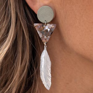 Könnte beinhalten: Ein Set aus drei Keramikbechern mit gesprenkelter, matter Oberfläche. Die Becher sind in den Farbtönen Creme, Hellgrau und Dunkelgrau gehalten. Jeder Becher hat ein schlichtes, minimalistisches Design, perfekt für Kaffee oder Tee.