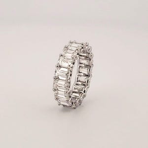 Peut inclure: Une bague alliance en métal argenté ornée d'une rangée continue de pierres transparentes rectangulaires taille baguette, serties dans une monture polie. Les pierres sont disposées verticalement sur toute la circonférence de l'anneau.