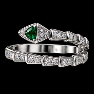 May include: A silver-toned snake-shaped ring featuring a triangular green gemstone set in the head. The body of the snake is segmented and encrusted with numerous small, clear, sparkling stones that cover the entire band and head design.