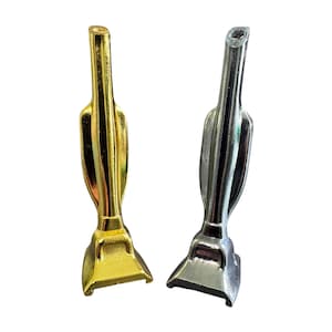 May include: Two miniature vacuum cleaner figurines. One is gold-coloured, the other is silver-coloured. Both have a similar design, with a rectangular base and a long, slender handle. The figurines are likely decorative items or part of a dollhouse set.