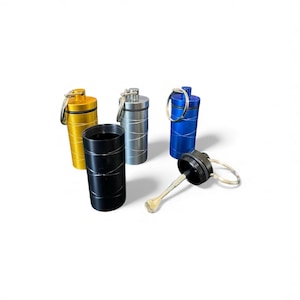May include: Four cylindrical metal containers with keyrings, featuring a spiral etched pattern on the exterior. The set includes gold, silver, blue, and black colors. One black container is open, revealing a small metal spoon attached to the lid.