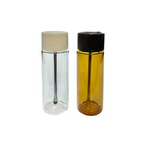 May include: Two small glass vials with attached applicators. One vial is clear with a cream cap, and the other is amber with a black cap. The vials are cylindrical and appear to be empty.