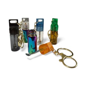 May include: A collection of small, colorful, and transparent bottles with keychains. The bottles come in various colors, including black, clear, blue, green, and iridescent. One bottle has a small spoon attached, and another has a metal tool.