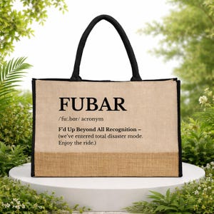 Puede incluir: Un bolso tote beige con asas y ribetes negros. La bolsa presenta la palabra "FUBAR" en letras grandes y en negrita, junto con su definición: "F'd Up Beyond All Recognition - (we've entered total disaster mode. Enjoy the ride.)"