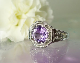 May include: A silver ring with an octagonal setting featuring a large, round, purple amethyst gemstone. The ring has a delicate, filigree design.