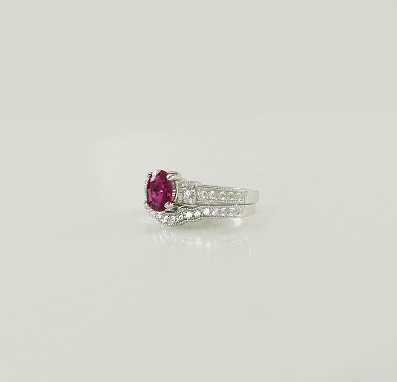 May include: A silver ring set with a large oval ruby gemstone and smaller diamonds. The ring is set on a white background.