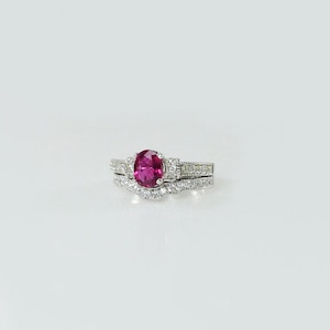 May include: A silver ring set with a pink oval gemstone surrounded by smaller clear gemstones.