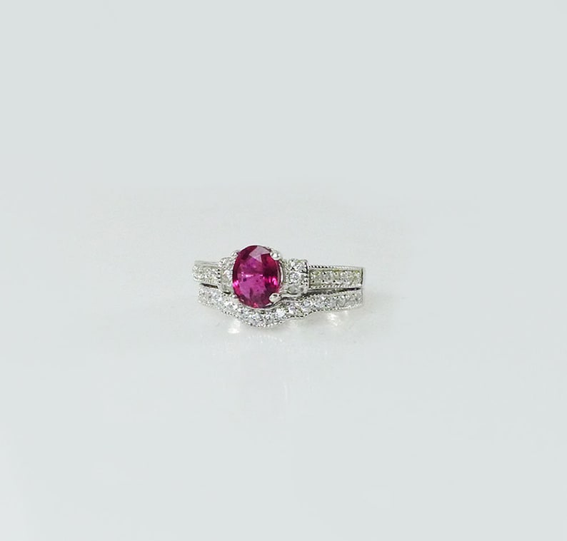 May include: A silver ring set with a pink oval gemstone surrounded by smaller clear gemstones.
