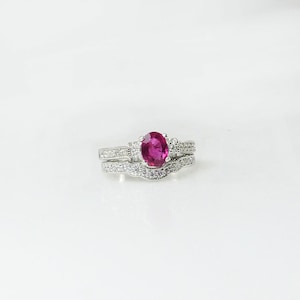 May include: A silver ring set with a large oval-shaped ruby gemstone surrounded by smaller clear gemstones.