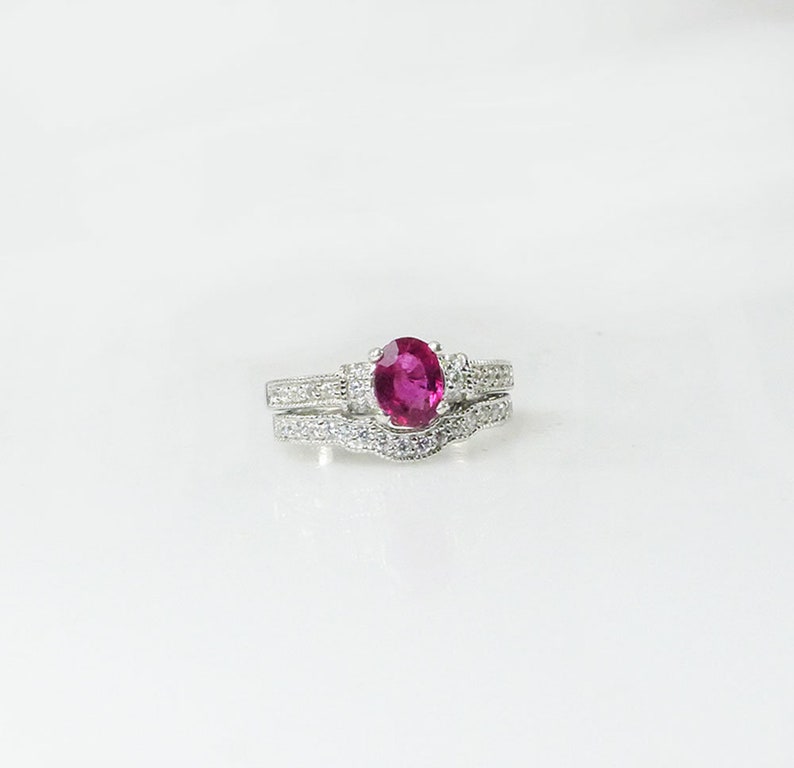 May include: A silver ring set with a large oval-shaped ruby gemstone surrounded by smaller clear gemstones.